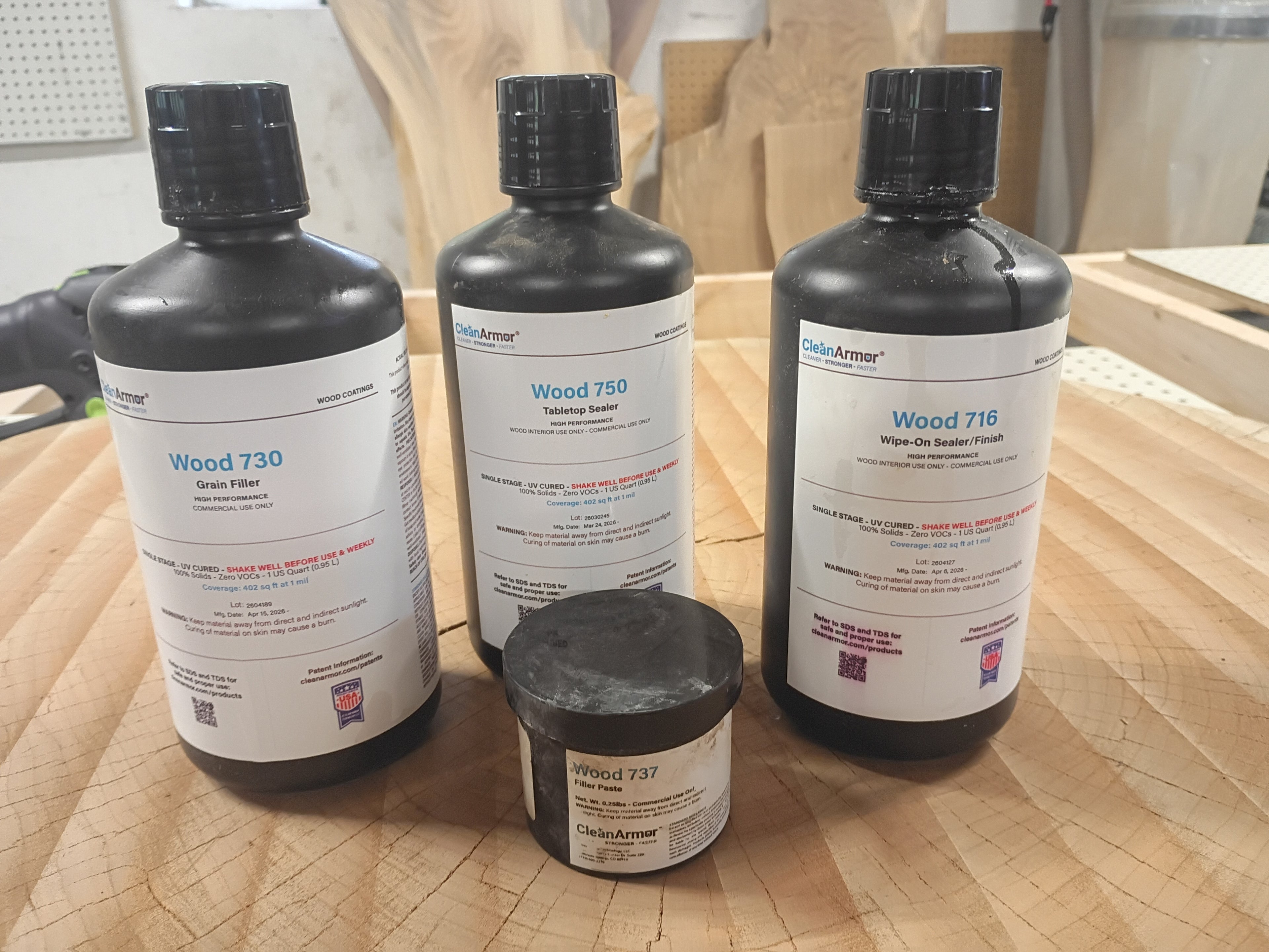 Three bottles and a jar of Wood Armor wood finish products on a wooden surface. Displaying what Jaeger Design LLC. is proudly using